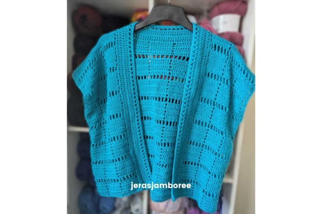 Front view of the turquoise Marlowe short sleeve summer crochet cardigan hanging on a black hanger, showing the open front, filet square stitch panels, and lightweight drape.