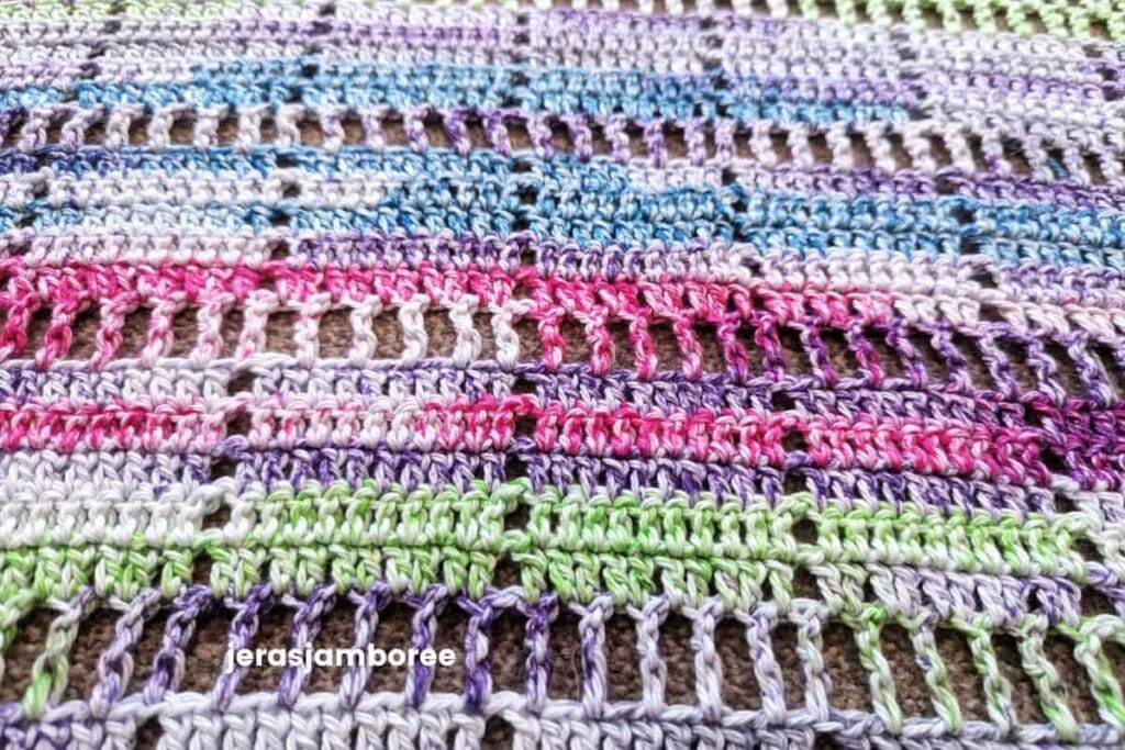 Close-up of the stitch detail on the Marlowe Summer Top crochet pattern, showing the airy filet crochet design worked in self-striping cotton yarn with pink, purple, blue, and green colour changes.