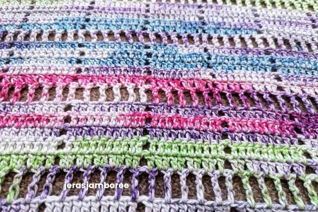 Close-up of the stitch detail on the Marlowe Summer Top crochet pattern, showing the airy filet crochet design worked in self-striping cotton yarn with pink, purple, blue, and green colour changes.