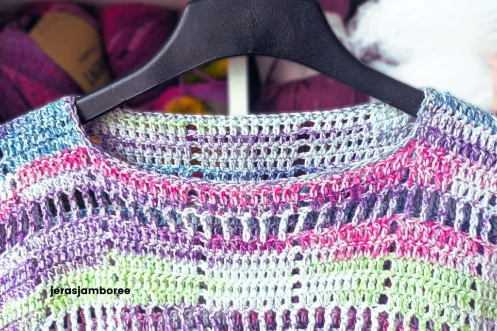 Close-up of the neckline and upper stitches on the Marlowe Summer Top crochet pattern, showing the lightweight filet crochet texture worked in a colourful self-striping cotton yarn with shades of pink, purple, blue, and green.