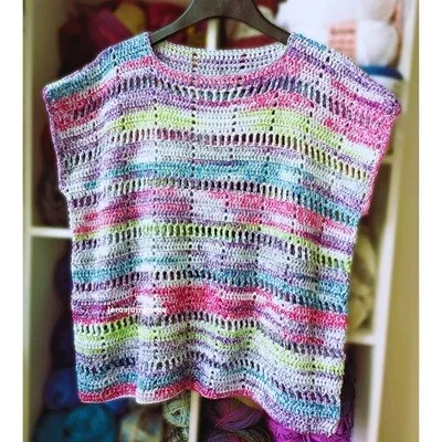 Handmade Marlowe Summer Top hanging on a black hanger, showing the lightweight filet crochet stitch pattern worked in colourful self-striping cotton yarn with pink, purple, blue, and green tones.
