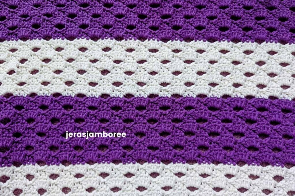 Close-up of the Arcade stitch used in the Coralie crochet poncho, showing the open shell pattern worked in alternating purple and cream stripes. This lightweight crochet stitch creates an airy fabric with beautiful drape for spring and summer garments.