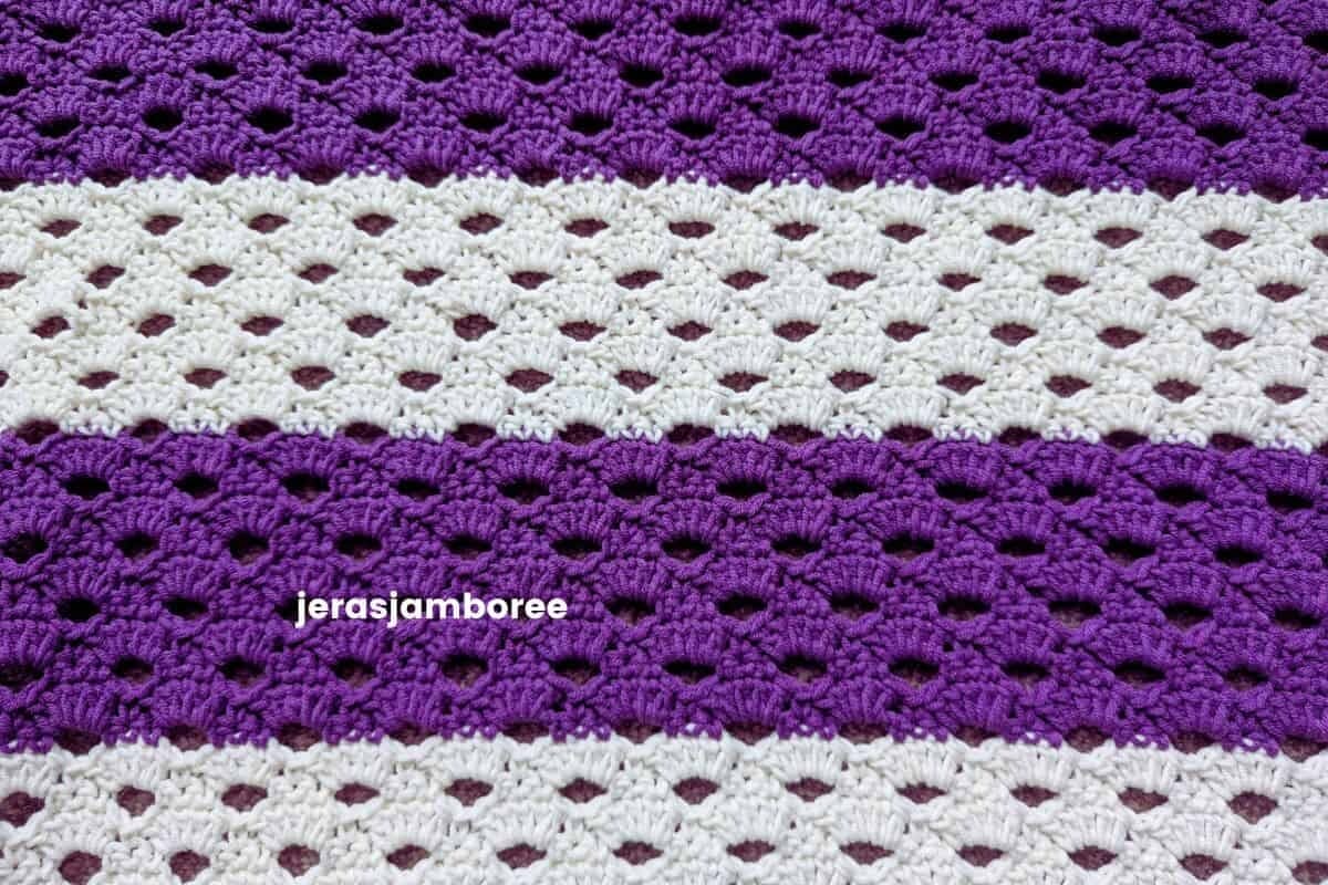 Close-up of the Arcade stitch used in the Coralie crochet poncho, showing the open shell pattern worked in alternating purple and cream stripes. This lightweight crochet stitch creates an airy fabric with beautiful drape for spring and summer garments.