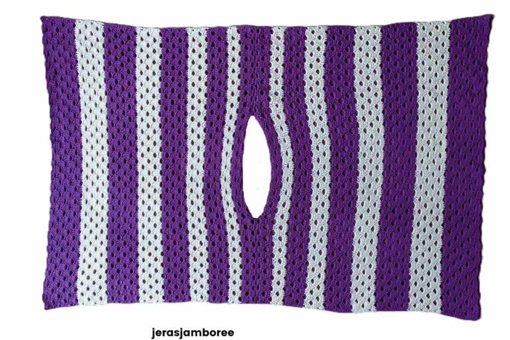 Flat lay of the Coralie crochet poncho showing the boat-neck opening and simple two-panel construction. Worked in purple and cream Arcade stitch stripes, this lightweight crochet poncho demonstrates how the neckline is formed before seaming the shoulders.