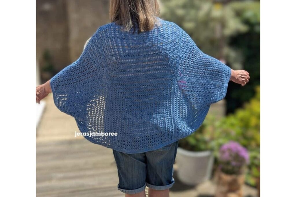 Back view of the Aveline Cocoon Cardigan worn with arms outstretched, showing the relaxed cocoon shape, oversized granny square construction and lightweight drape of the blue crochet fabric.