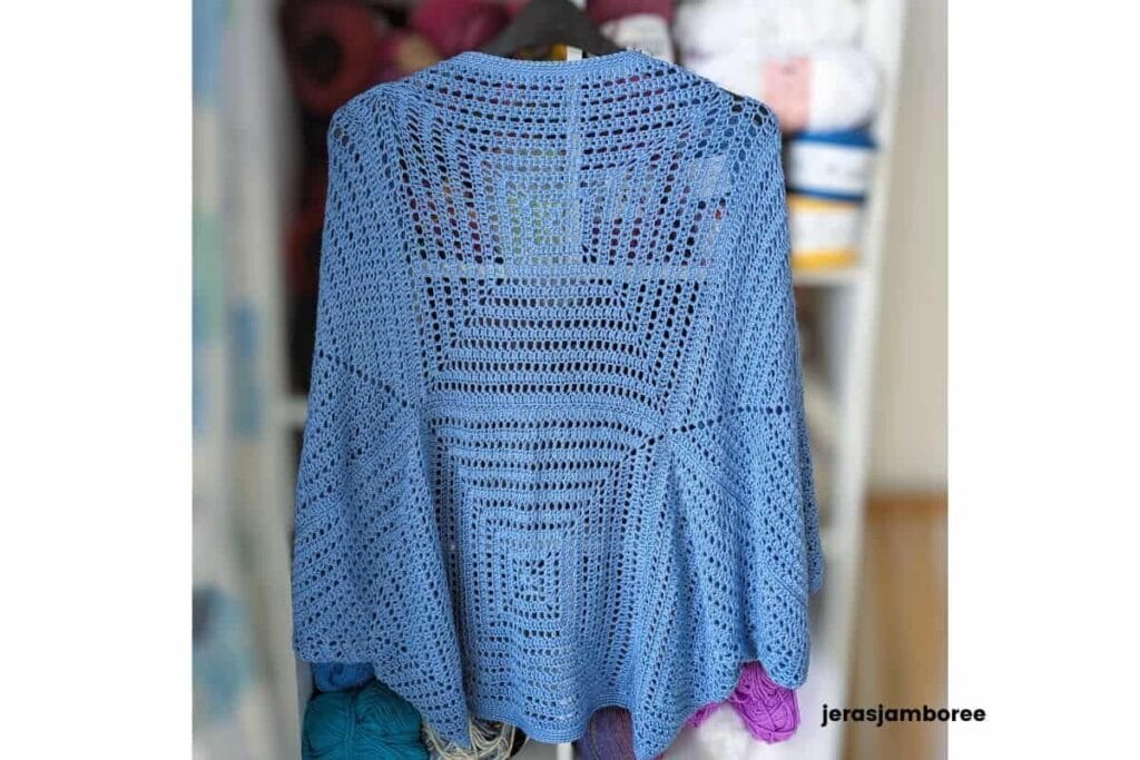 Back view of the Aveline Cocoon Cardigan hanging on a hanger, showing the six oversized granny square construction, lightweight drape and relaxed cocoon silhouette in soft blue DK bamboo yarn.