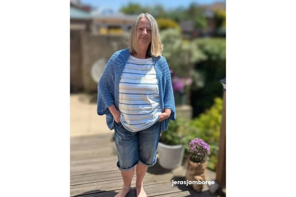 the Aveline Granny Square Shrug worn over a striped top, showing the open-front cocoon shape, oversized granny square construction and lightweight drape of the blue crochet fabric.