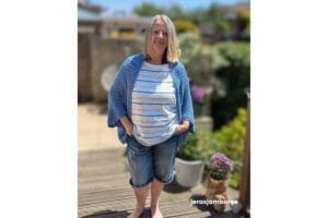 the Aveline Granny Square Shrug worn over a striped top, showing the open-front cocoon shape, oversized granny square construction and lightweight drape of the blue crochet fabric.
