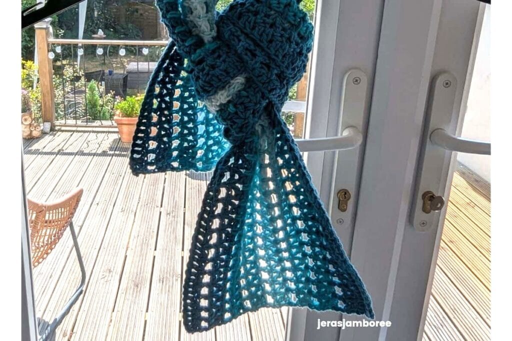 The Sandrine Scarf tied loosely, showing the lightweight drape, open mesh stitch and blue striped colour changes.