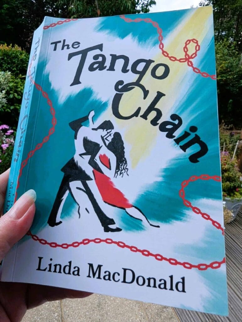 The Tango Chain by Linda MacDonald paperback book cover held outdoors in a garden.