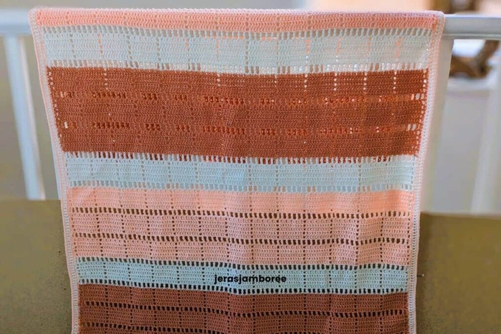 Marlowe crochet lap blanket displayed over a bannister, showing the geometric filet blocks, open mesh rows and three-colour design.