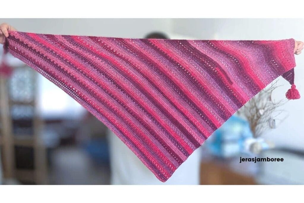 Mariselle bias crochet shawl held open to show its asymmetric shape and diagonal stripes in pink and purple self-striping yarn