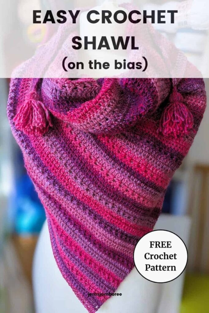 Mariselle easy crochet shawl worked on the bias in pink and purple self-striping yarn, shown draped on a mannequin with tassels.